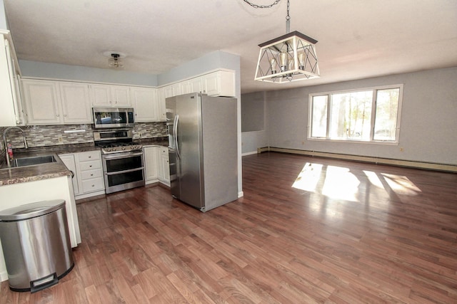 kitchen with stainless steel appliances, dark countertops, hanging light fixtures, white cabinets, and a sink