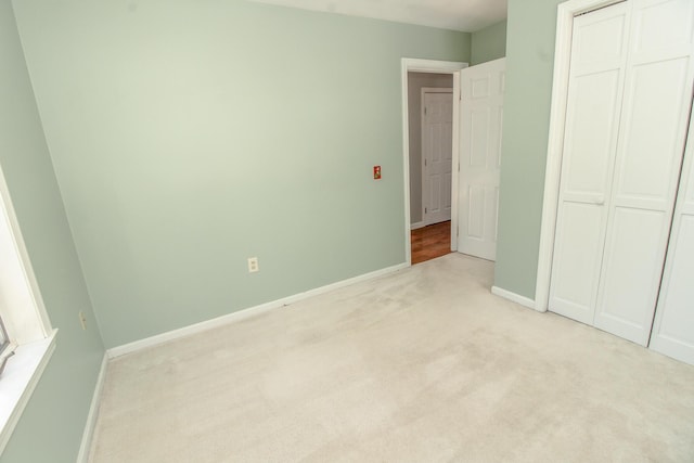 unfurnished bedroom featuring a closet, light carpet, and baseboards