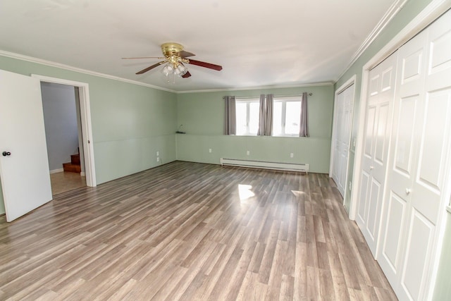 unfurnished bedroom featuring multiple closets, crown molding, light wood-style floors, and baseboard heating