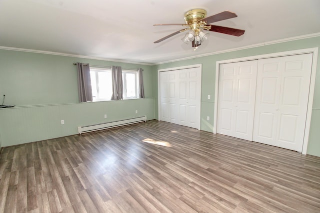 unfurnished bedroom with multiple closets, ornamental molding, baseboard heating, and wood finished floors