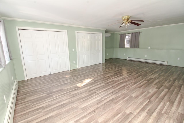 unfurnished bedroom with a baseboard radiator, wood finished floors, crown molding, a baseboard heating unit, and two closets