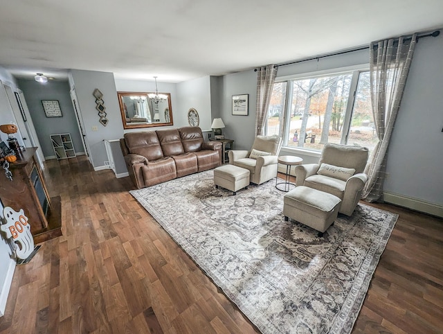 living area featuring dark wood-type flooring, a notable chandelier, and baseboards