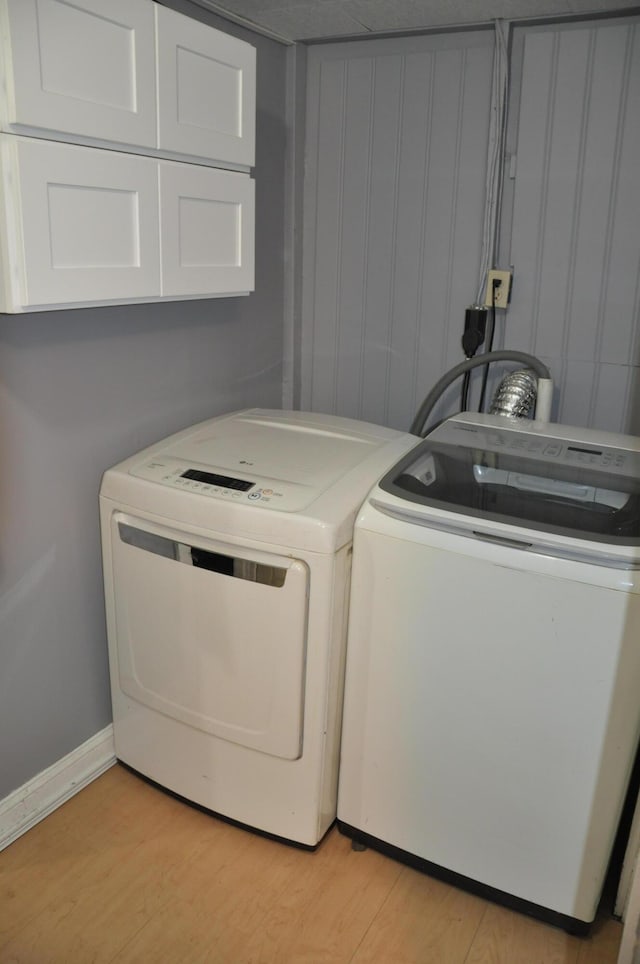 washroom featuring baseboards, cabinet space, washing machine and clothes dryer, and light wood finished floors