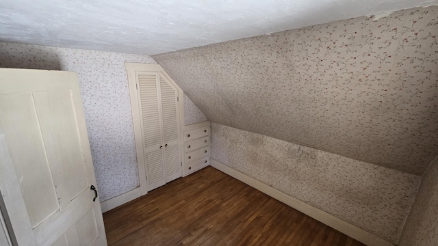 additional living space with lofted ceiling, dark wood-style flooring, baseboards, and wallpapered walls