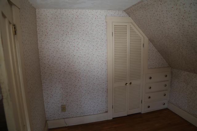 additional living space featuring dark wood-type flooring, lofted ceiling, and wallpapered walls