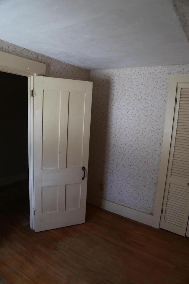 empty room with baseboards, dark wood finished floors, and wallpapered walls