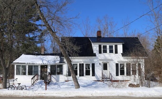 snow covered back of property with entry steps and a chimney