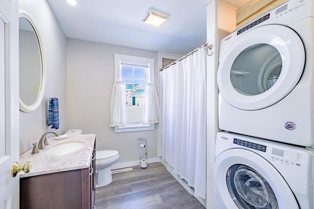 laundry area with light wood finished floors, stacked washer / dryer, a sink, laundry area, and baseboards