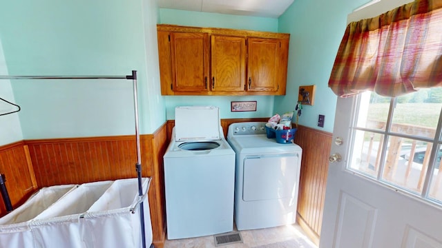 laundry room featuring cabinet space, wooden walls, visible vents, wainscoting, and washing machine and clothes dryer