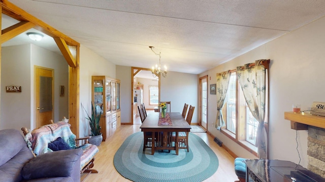 dining area with a wealth of natural light, light wood-style flooring, a textured ceiling, and an inviting chandelier