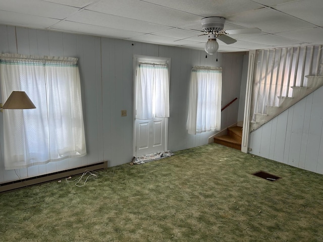 empty room with ceiling fan, a baseboard heating unit, carpet flooring, visible vents, and stairway