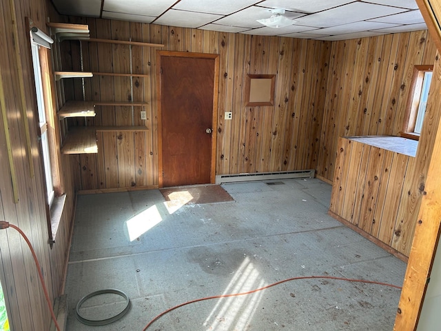 unfurnished room with a baseboard radiator, a paneled ceiling, and wood walls