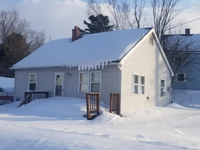 snow covered rear of property with a chimney