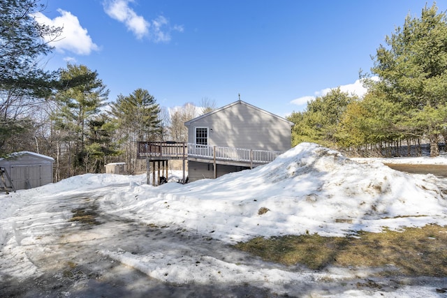 snow covered property with a storage unit, a deck, and an outdoor structure