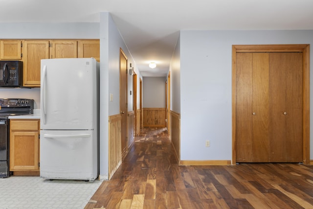 kitchen featuring a wainscoted wall, black appliances, dark wood finished floors, and light countertops