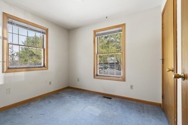 carpeted spare room featuring a healthy amount of sunlight, baseboards, and visible vents