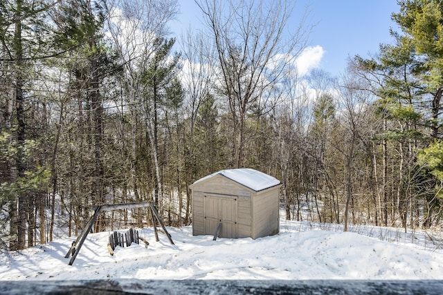 yard covered in snow featuring a storage unit, a wooded view, and an outdoor structure