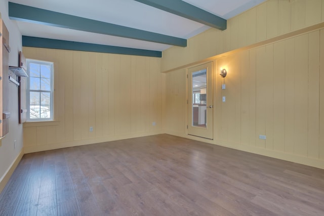 empty room featuring baseboards, beamed ceiling, and wood finished floors