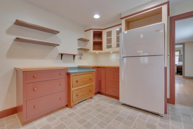 kitchen with baseboards, light countertops, freestanding refrigerator, open shelves, and glass insert cabinets