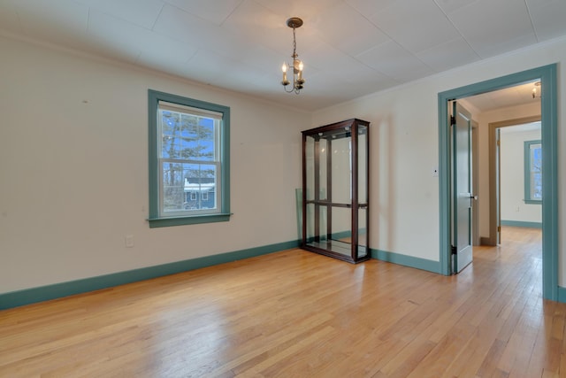 empty room with light wood-style floors, a chandelier, ornamental molding, and baseboards