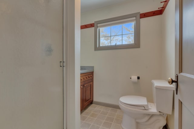 bathroom with toilet, a shower stall, baseboards, and vanity