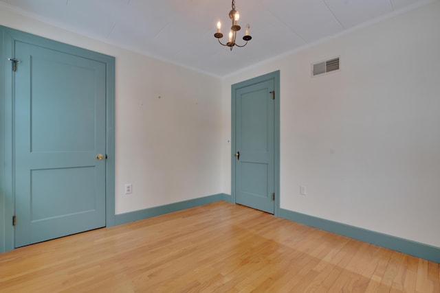 unfurnished room with light wood finished floors, baseboards, visible vents, and an inviting chandelier