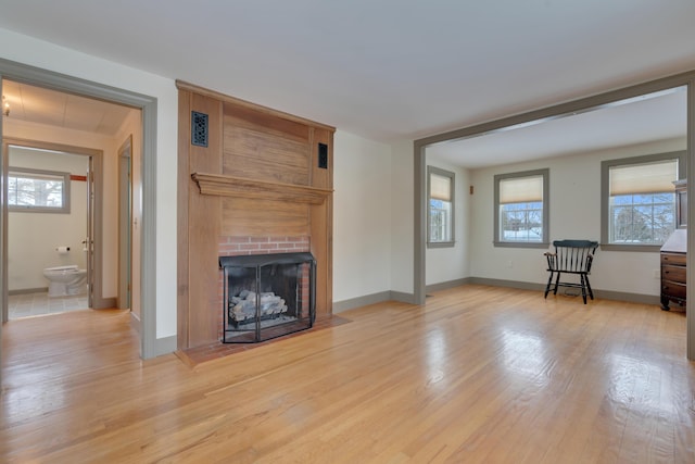 unfurnished living room featuring light wood finished floors, a brick fireplace, and baseboards