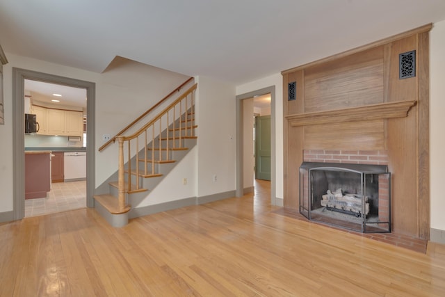 unfurnished living room featuring light wood-style flooring, a fireplace, visible vents, baseboards, and stairs