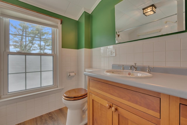 bathroom with toilet, wood finished floors, vanity, tile walls, and crown molding