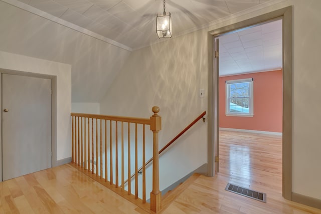 hall featuring light wood-type flooring, baseboards, visible vents, and an upstairs landing