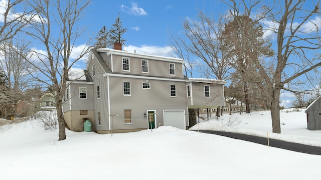 snow covered rear of property featuring an attached garage and a chimney