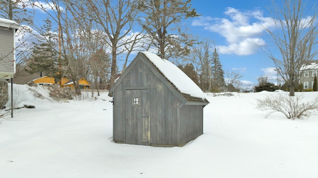 snow covered structure featuring a garage, an outdoor structure, and a shed