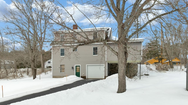 snow covered house featuring a garage and a chimney