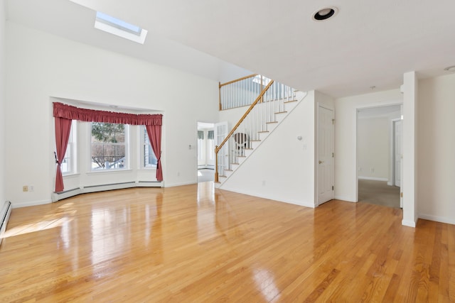 unfurnished living room featuring light wood-style floors, a baseboard radiator, a skylight, and stairs