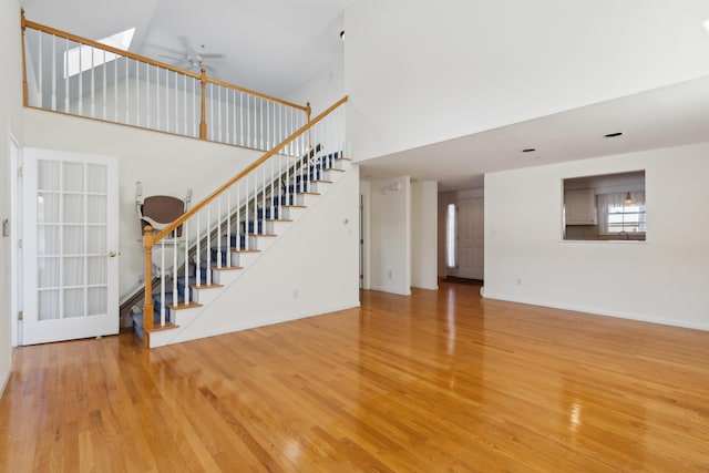 unfurnished living room with wood finished floors, ceiling fan, a high ceiling, and stairs