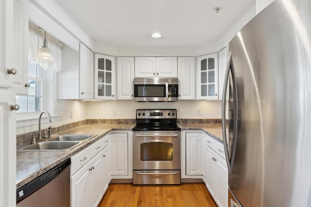 kitchen with light wood finished floors, stainless steel appliances, glass insert cabinets, white cabinetry, and a sink