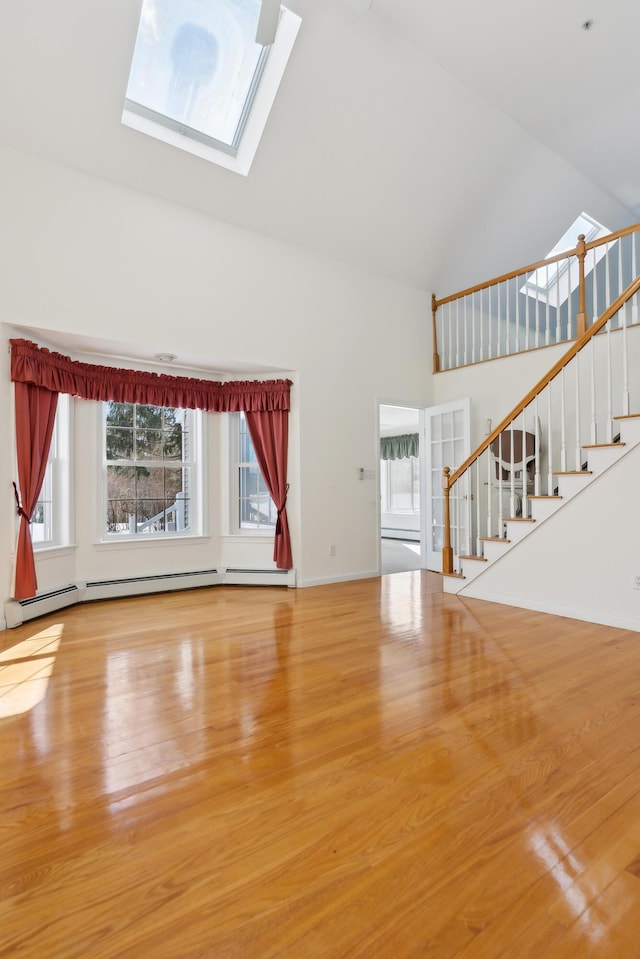 unfurnished living room featuring a skylight, a baseboard radiator, a wealth of natural light, stairway, and high vaulted ceiling