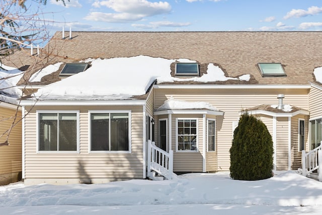 snow covered house with entry steps and a shingled roof