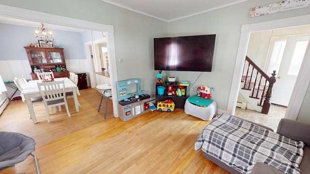 living area featuring a baseboard radiator, an inviting chandelier, stairs, crown molding, and light wood-type flooring