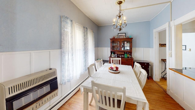 dining area with light wood finished floors, wainscoting, heating unit, and a notable chandelier