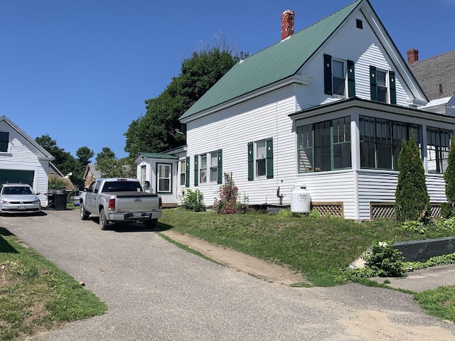 view of side of home with aphalt driveway, a sunroom, metal roof, and a chimney