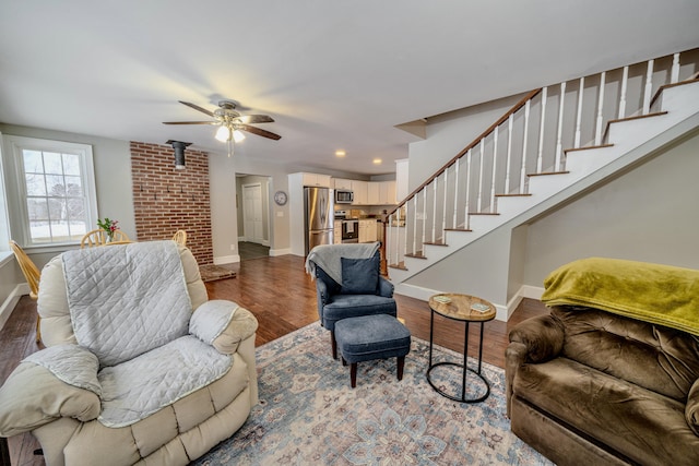 living room featuring wood finished floors, ceiling fan, baseboards, and stairs