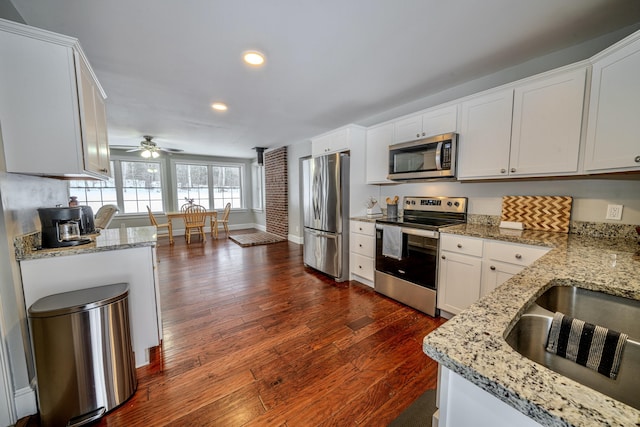 kitchen with dark wood-style floors, appliances with stainless steel finishes, white cabinets, a sink, and light stone countertops