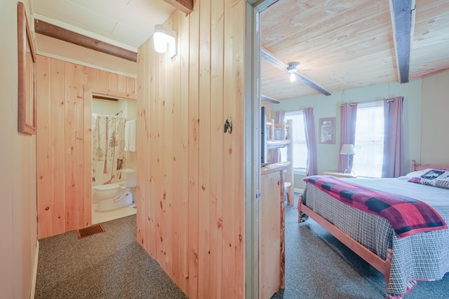 carpeted bedroom with connected bathroom, wooden ceiling, beamed ceiling, and wood walls