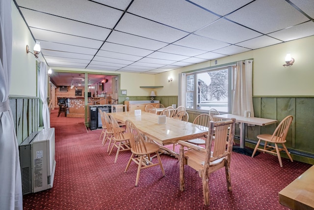 dining area with a paneled ceiling, a wainscoted wall, baseboard heating, and carpet flooring