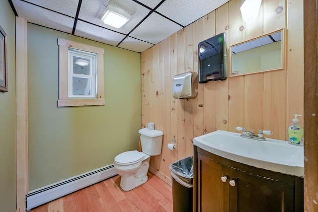 bathroom with toilet, a baseboard heating unit, vanity, wood finished floors, and a drop ceiling