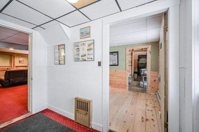 corridor with a wainscoted wall, hardwood / wood-style floors, and a drop ceiling