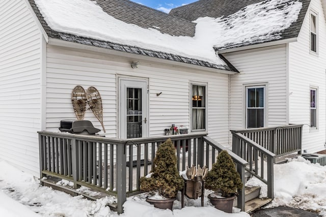 snow covered property entrance featuring roof with shingles