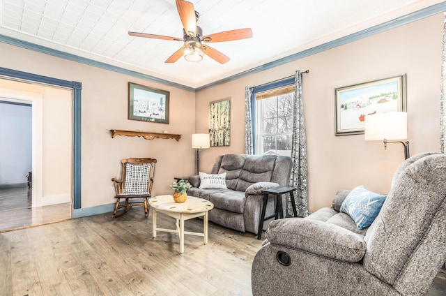 living area featuring a ceiling fan, light wood-type flooring, crown molding, and baseboards