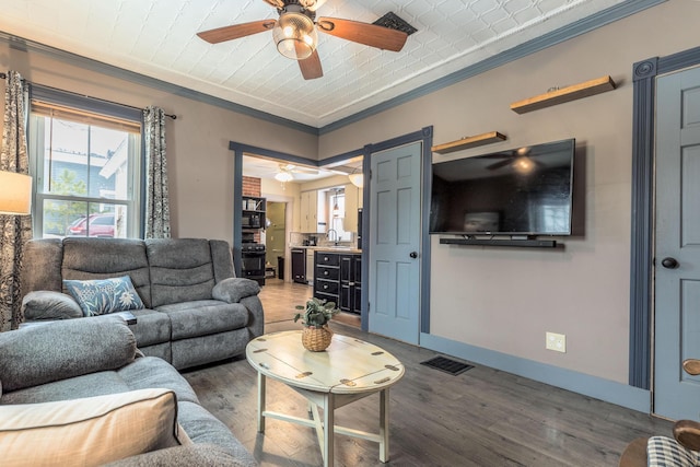 living room featuring ornamental molding, a ceiling fan, visible vents, and baseboards